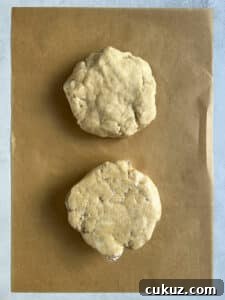 Two disks of pie dough on a piece of parchment - one wrapped in plastic wrap and one not.