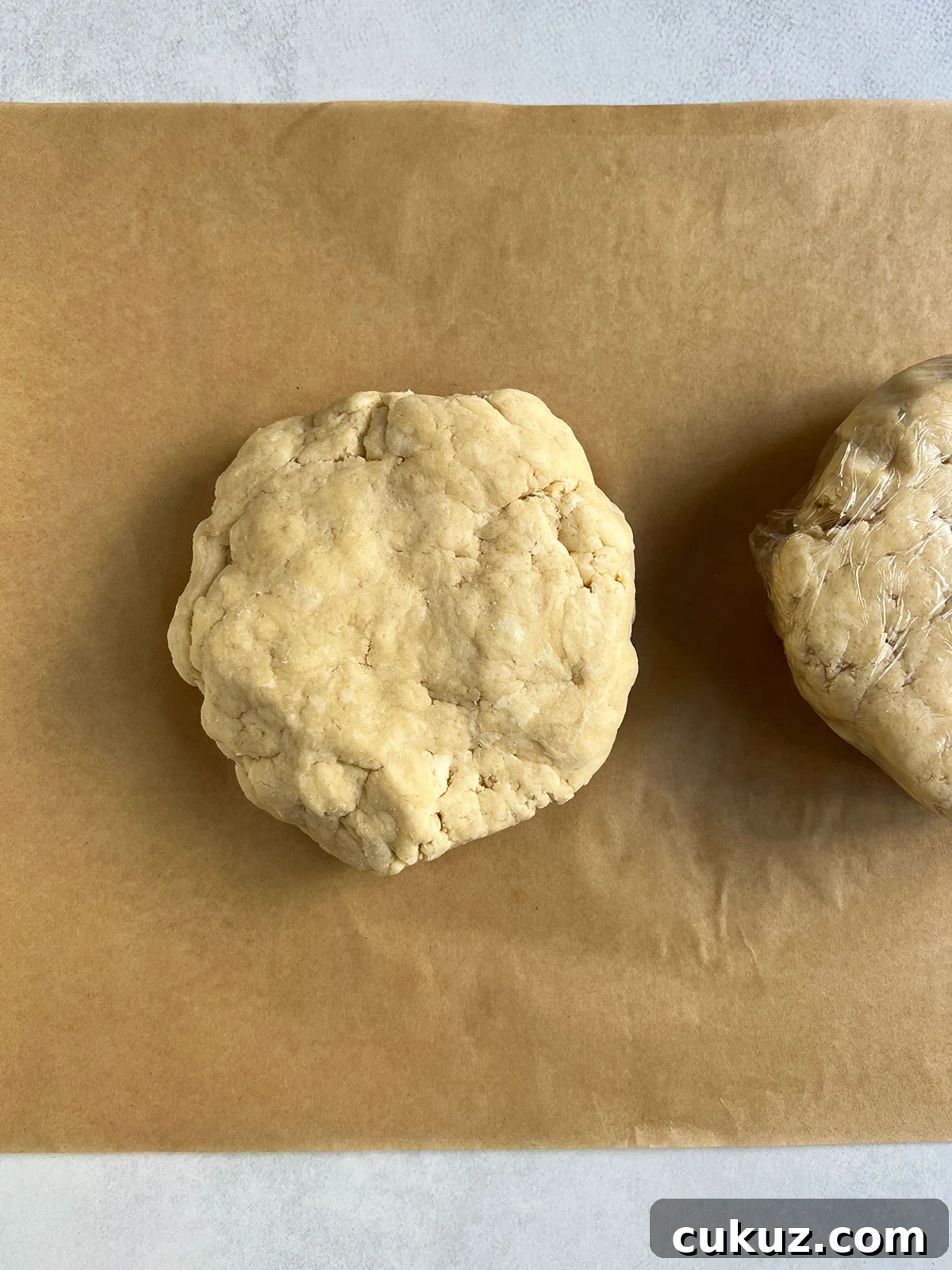 Disk of pie dough on parchment with a wrapped disk to the side partially showing.