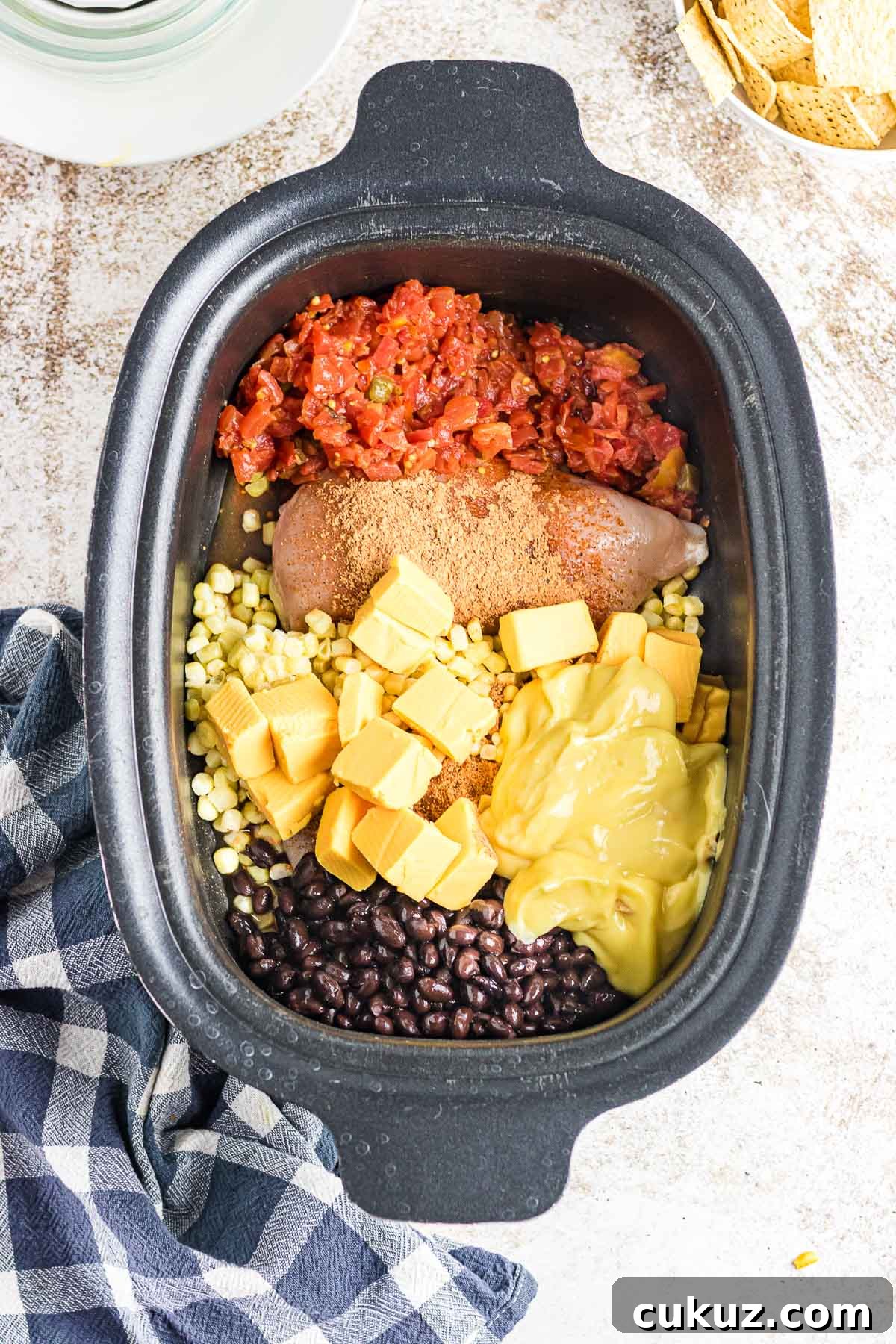A crockpot filled with chicken, tomatoes, corn, cheese, and beans.