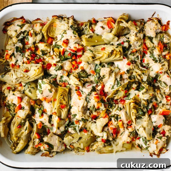 Spinach artichoke chicken bake in a pan next to wooden spoons