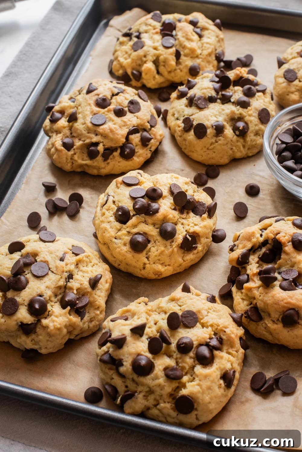 Freshly baked thick chocolate chip cookies cooling on a parchment-lined baking tray.