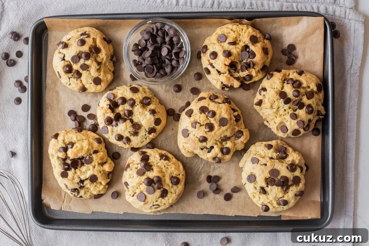 Overhead view of chocolate chip cookies arranged on a baking sheet with chocolate chips scattered around.