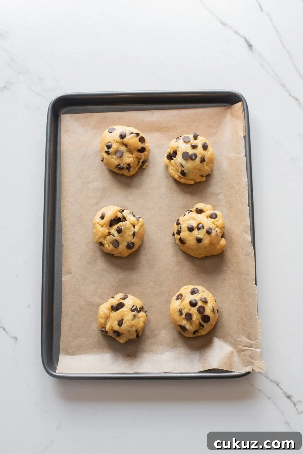 Tall mounds of chocolate chip cookie dough scooped onto a parchment-lined baking sheet.