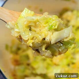 A wooden spoon holding stewed cabbage above a pot filled with more tender, cooked cabbage.