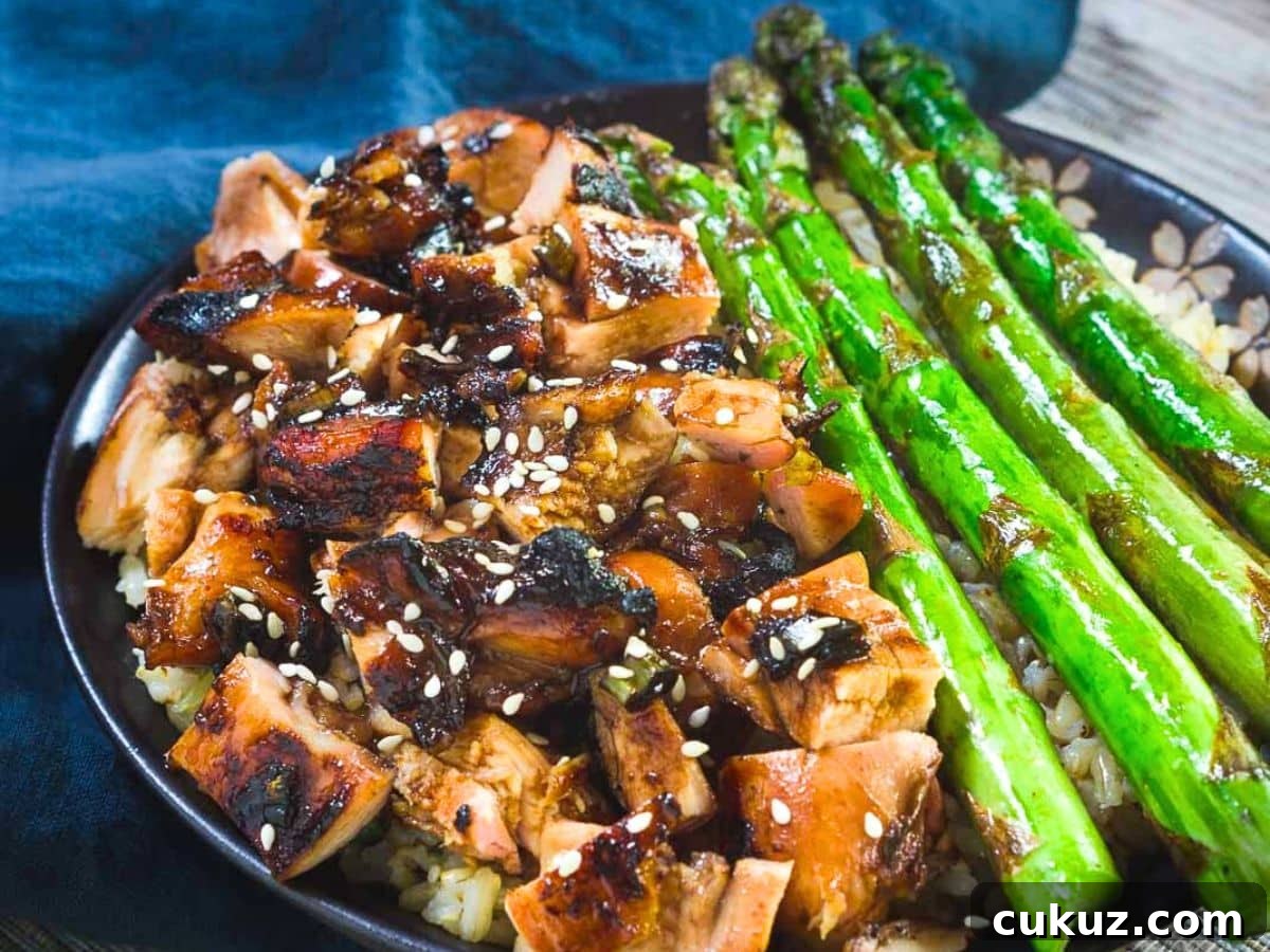 Sticky Teriyaki Grilled Chicken Bowl with Jasmine Rice 2 Angled view of a bowl filled with grilled chicken teriyaki and asparagus over brown rice and garnished with sesame seeds - Hostess At Heart