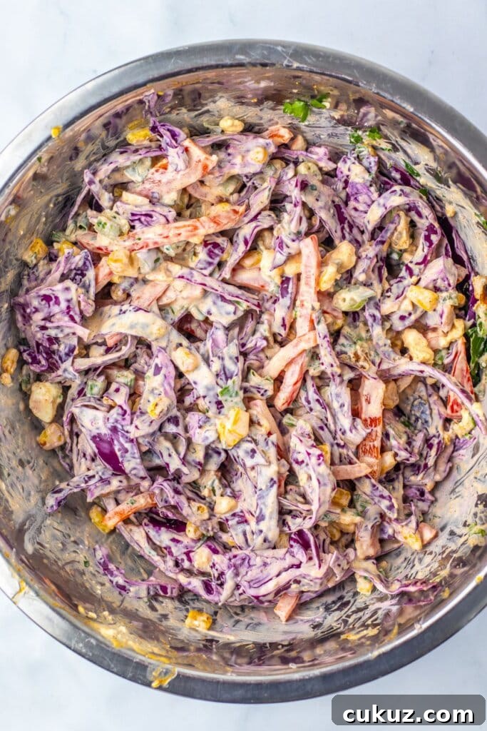 Coleslaw being mixed in a stainless steel mixing bowl.