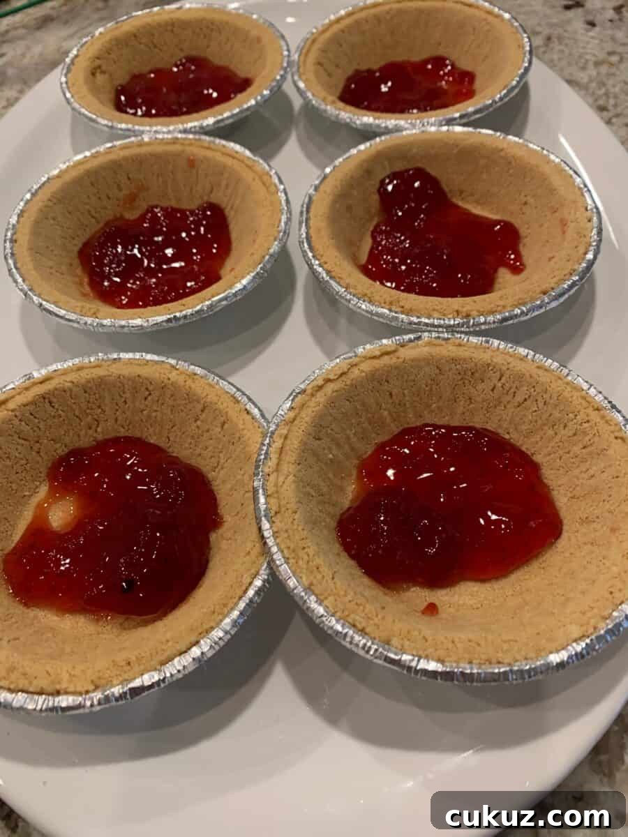 A layer of strawberry jam in the bottom of six mini pie crusts.