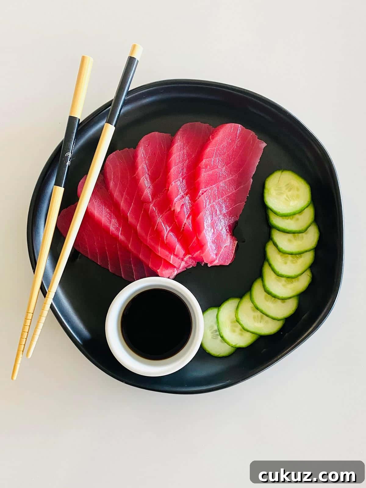 ahi tuna sashimi on plate with soy sauce, sliced cucumbers and chopsticks.
