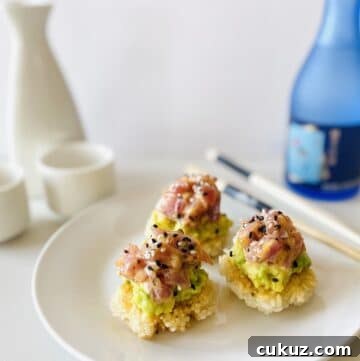 spicy tuna crispy rice on plate next to chopsticks, sake and sake carafe and glasses