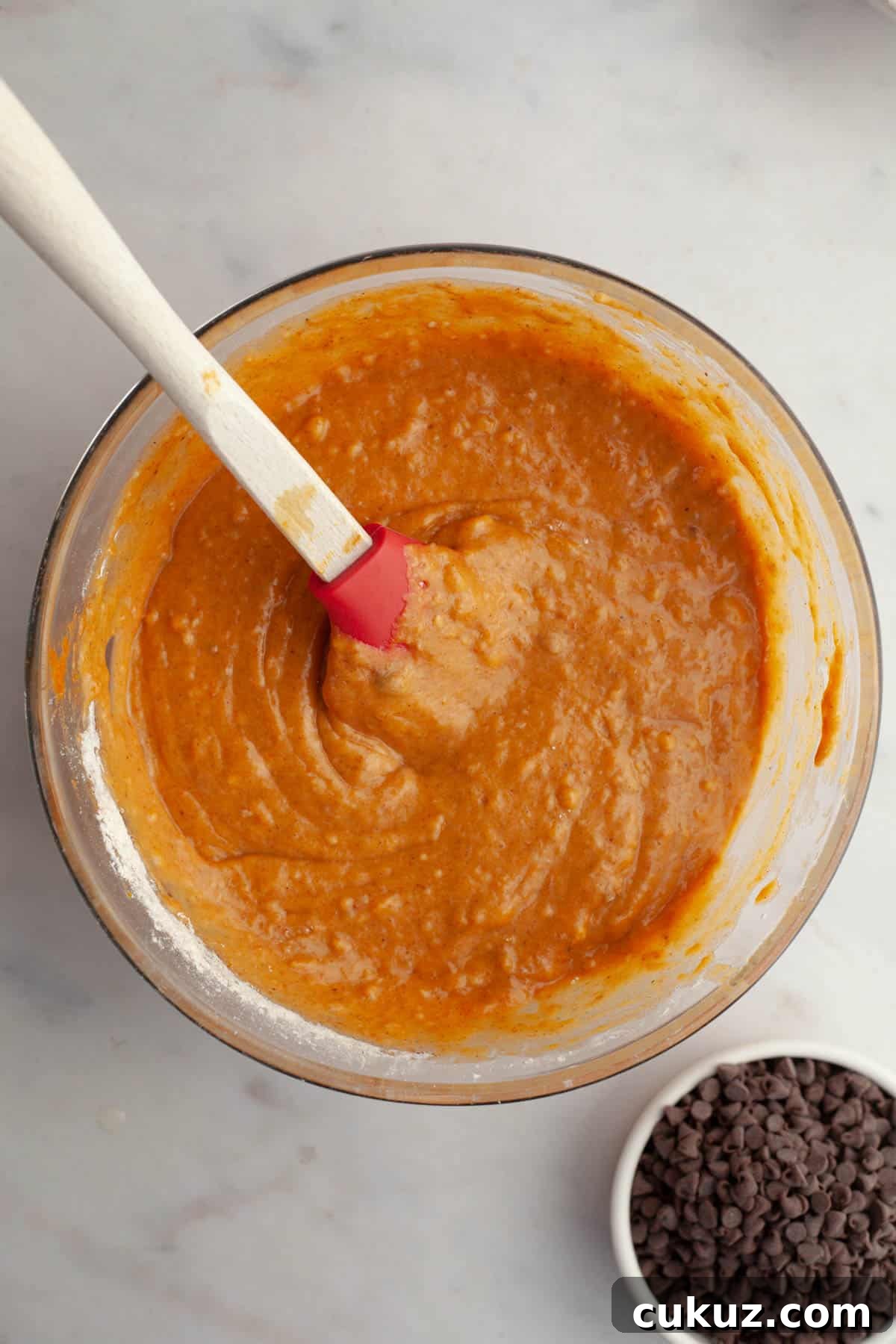 Pumpkin muffin batter in a glass bowl with a spatula.