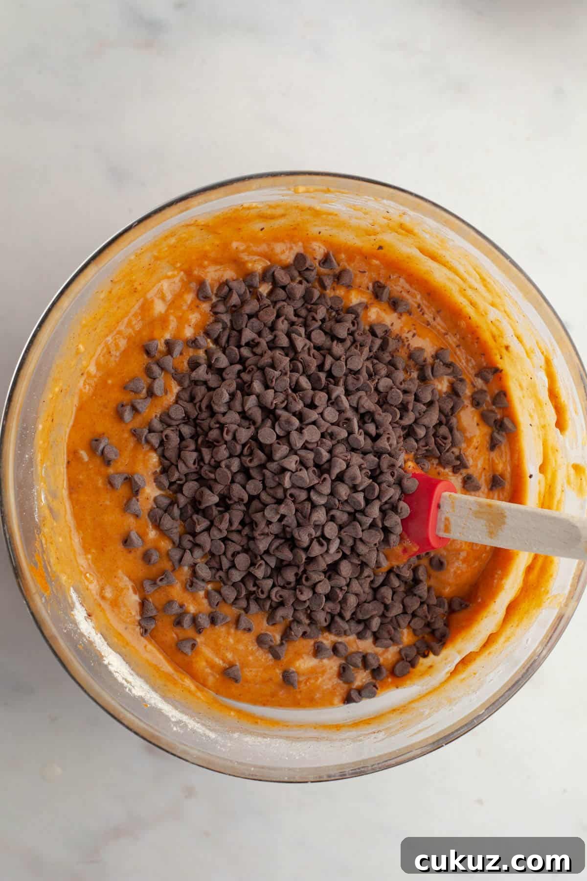 A glass bowl with pumpkin muffin batter and mini chocolate chips.