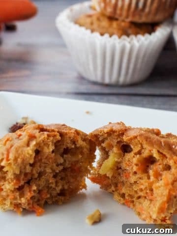 carrot muffin on blue wood-like surface, pulled into 2 pieces , with wrapper, more muffins and carrots in background