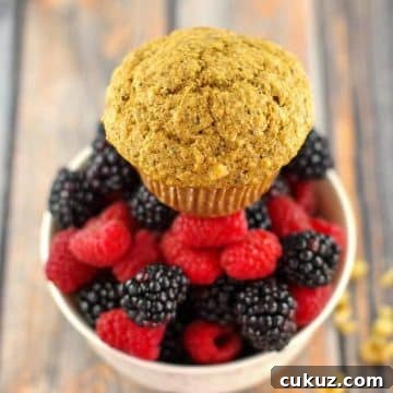 A Wheat Bran Muffins sitting on top of a bowl of fresh mixed berries, with walnuts scattered beside the bowl.