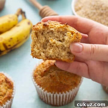 half an oat bran muffin being held up over a full muffin with bananas in the background